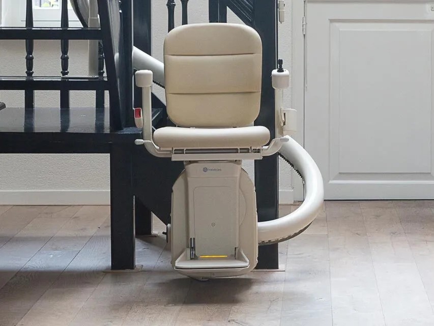 A cream single-tube Freecurve stairlift at the foot of a curved black staircase